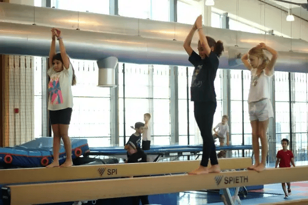3 girls on a balance beam with their arms stretched upwards
